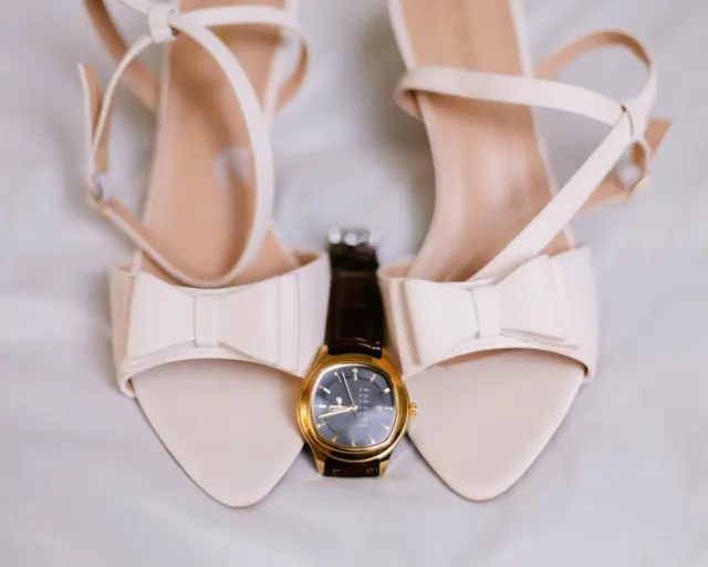Wedding shoes and a watch arranged on soft fabric